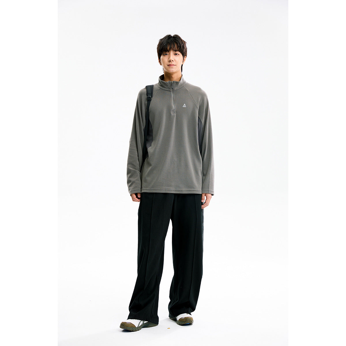 Full-length model wearing a gray quarter-zip pullover and loose black trousers against a white studio background.