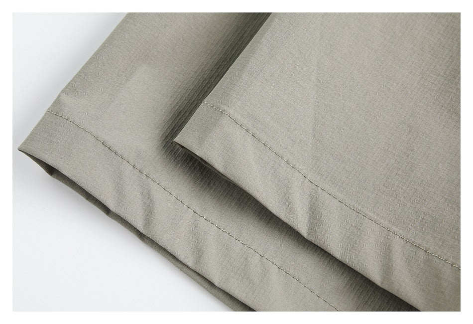 Close-up of light gray garment fabric and stitched hems along overlapping edges.