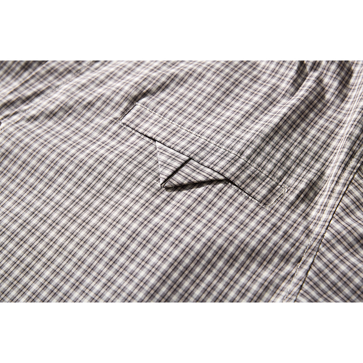 Close-up of a welt chest pocket on a gray, black, and cream checked shirt.