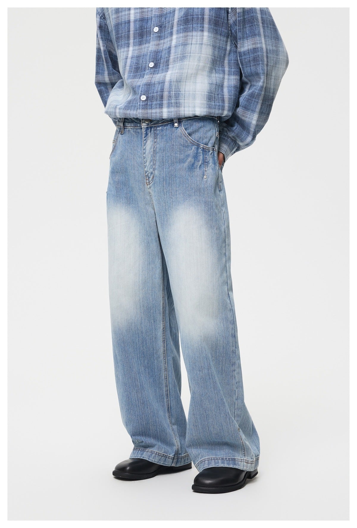 Cropped front view of a person wearing light blue faded, wide-leg jeans with a blue plaid shirt and black shoes.