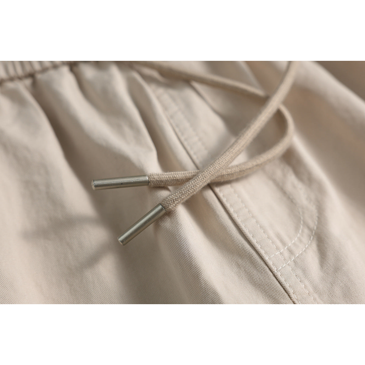 Close-up of beige shorts showing braided drawstrings with metal tips and the front pocket stitching.