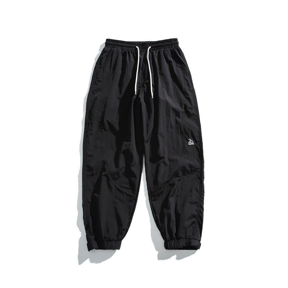 Black jogger pants flat lay with white drawstring, elastic cuffs and small embroidered logo
