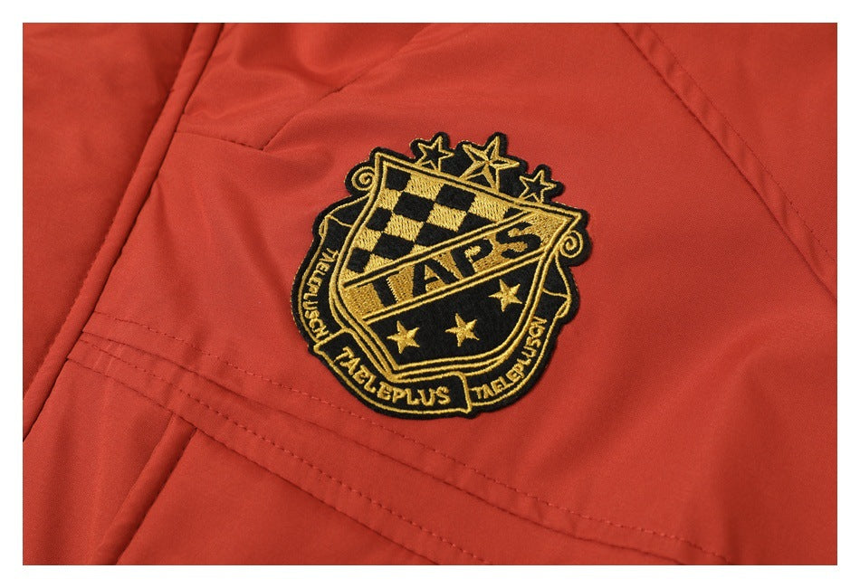 Close-up of a black-and-gold embroidered crest on rust-red coat fabric.