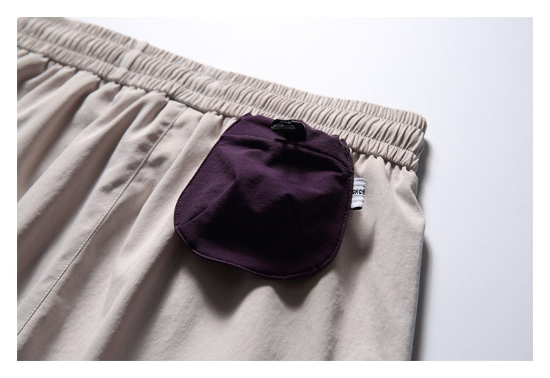 Close-up of pale gray shorts with a gathered elastic waistband and a rounded dark plum pocket with a small side tag.