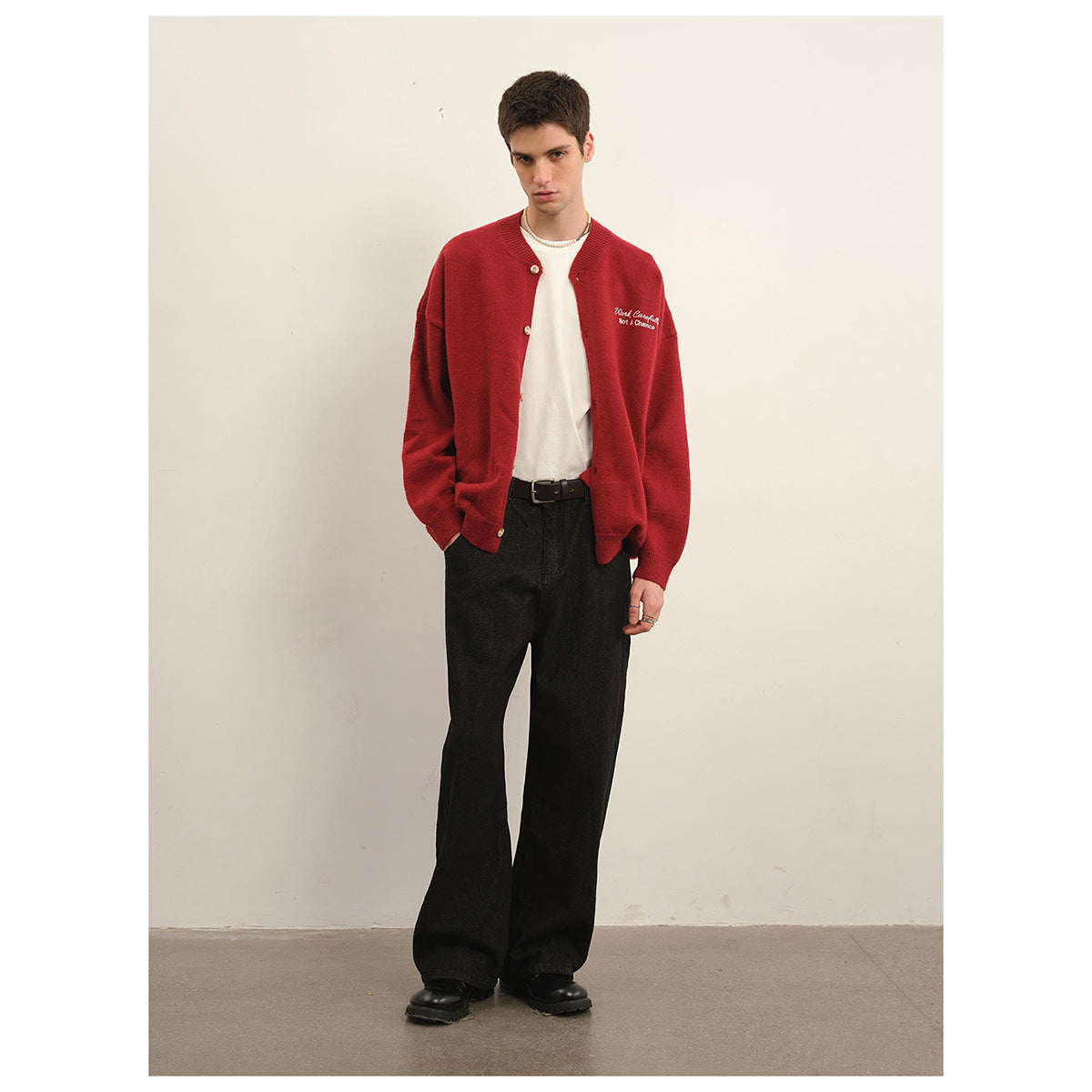 Model wearing a red button-front cardigan over a white shirt with loose black trousers, shown full length.