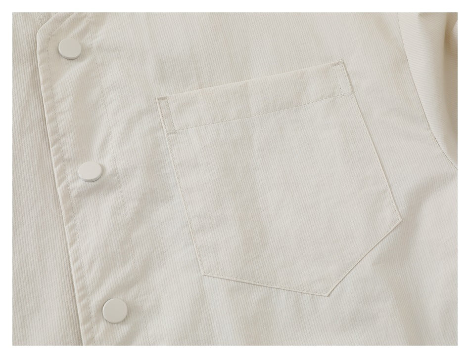 Close-up of an ivory garment's snap-button front and angular patch pocket.