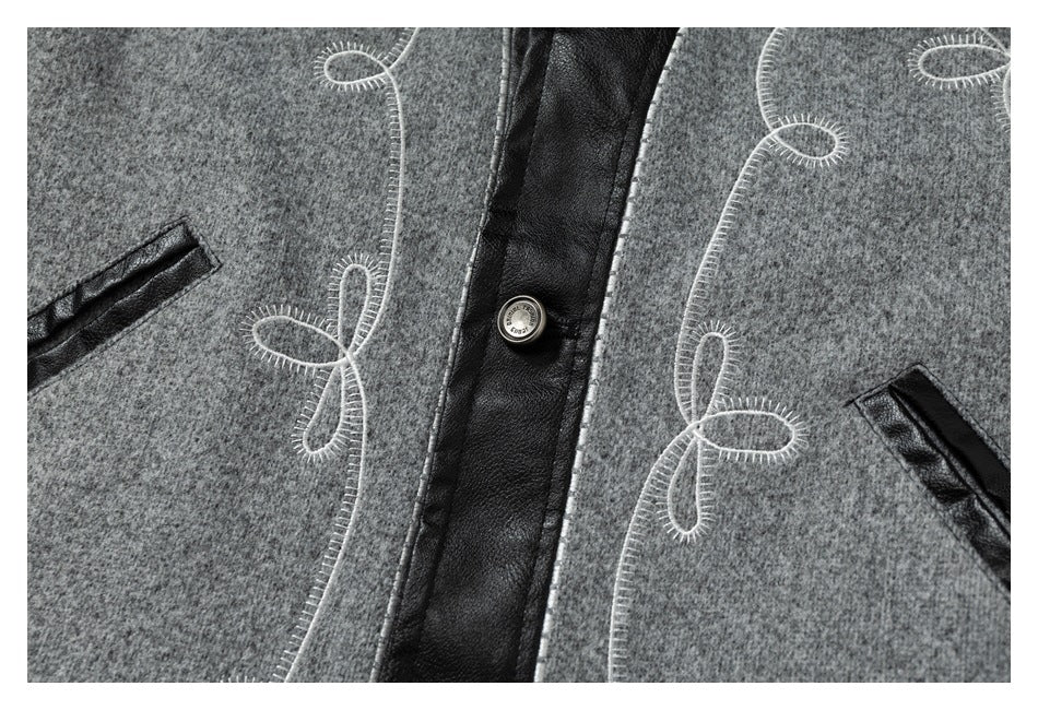 Close-up of a gray jacket front with black trim, white loop embroidery, pockets, and a metal button.