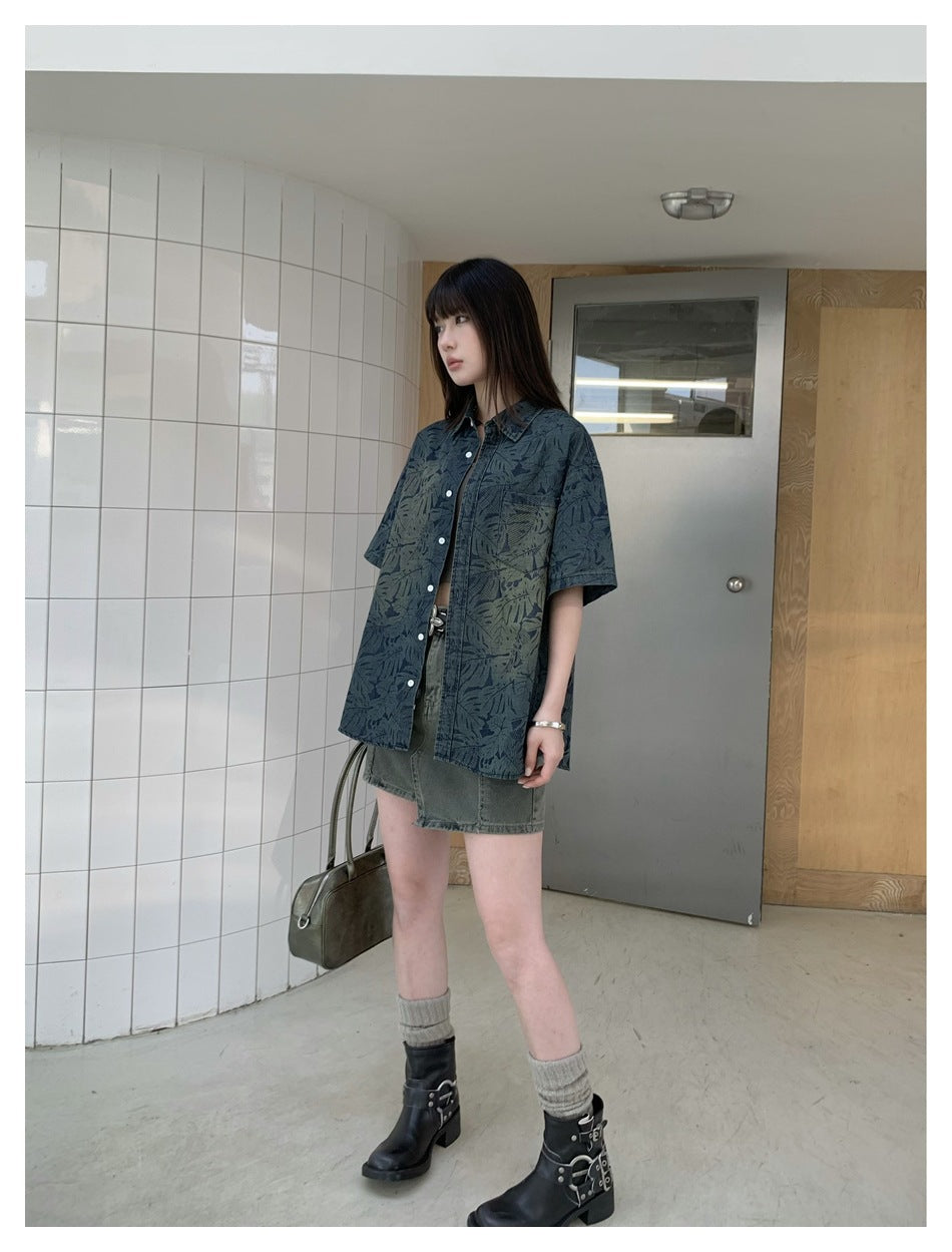 Model wearing an oversized dark blue-green short-sleeve button-up shirt with a leaf print and a pointed collar.