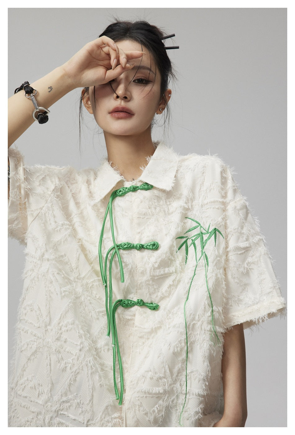 Close-up of an ivory textured jacket showing green frog closures and bamboo embroidery.