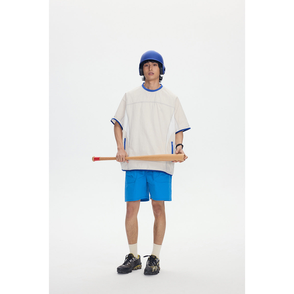 Full-length model wearing an ivory shirt with blue trim and blue shorts, holding a baseball bat.