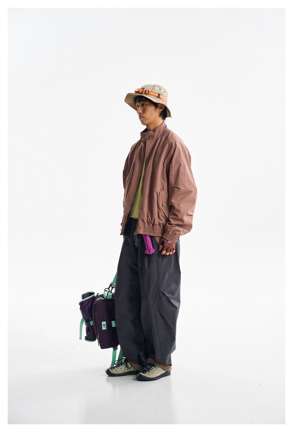 Model in a rose checked jacket and loose dark checked trousers, carrying a purple and mint bag.