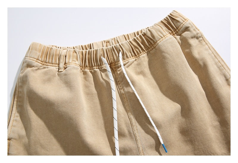 Close-up of tan trousers showing the gathered elastic waistband, belt loops, and white drawstrings.
