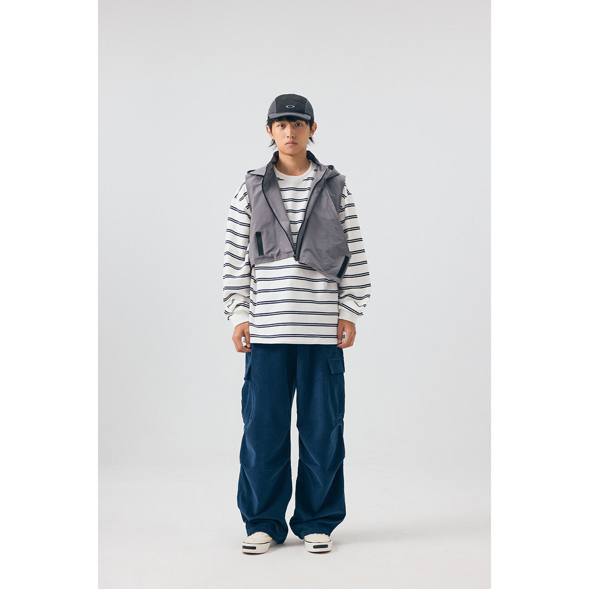 Full-length model wearing a gray hooded vest over a striped shirt with navy cargo pants.