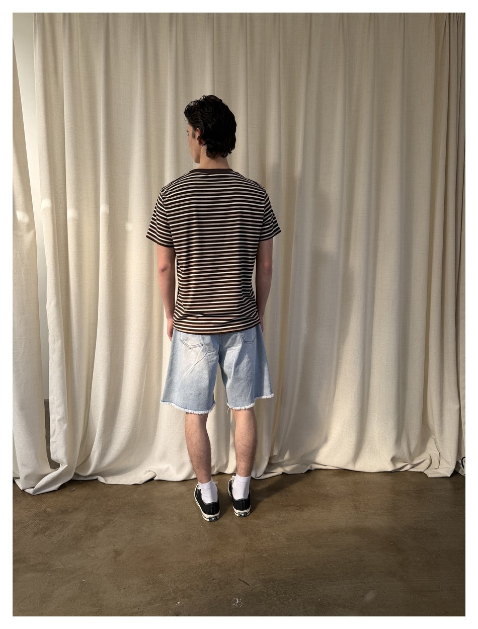 Back view of a model wearing a brown striped T-shirt with light denim shorts and black sneakers