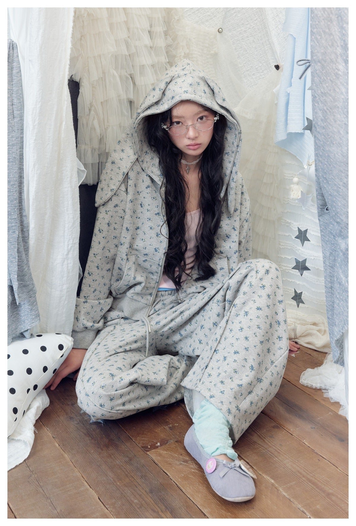 Seated model wearing a gray-blue floral-print zip hoodie and matching drawstring pants.