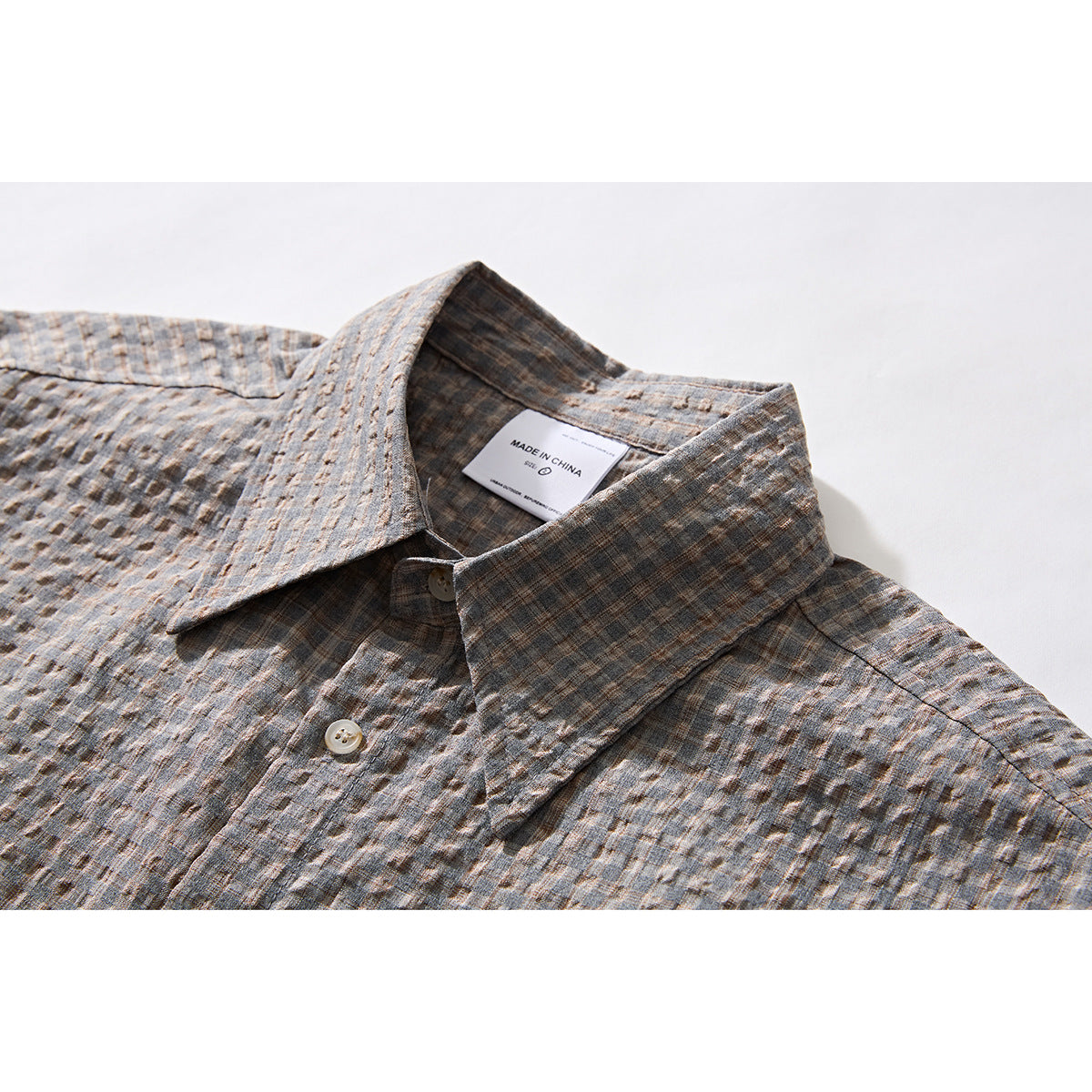 Close-up of a gray-brown textured plaid shirt collar, button placket, and sewn-in label.