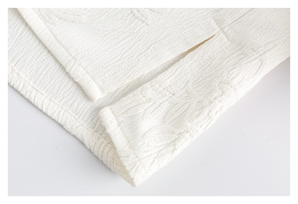 Close-up of a folded edge and stitched seams on white floral-textured fabric.