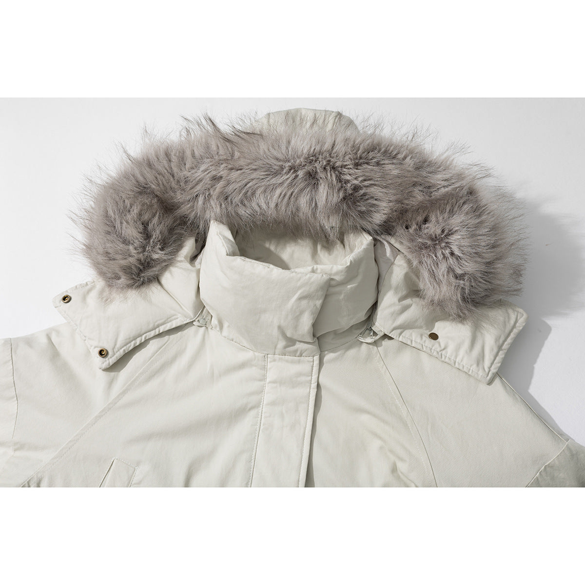 Close-up of an ivory coat’s high collar and hood with gray fur trim and snap-fastened tabs.