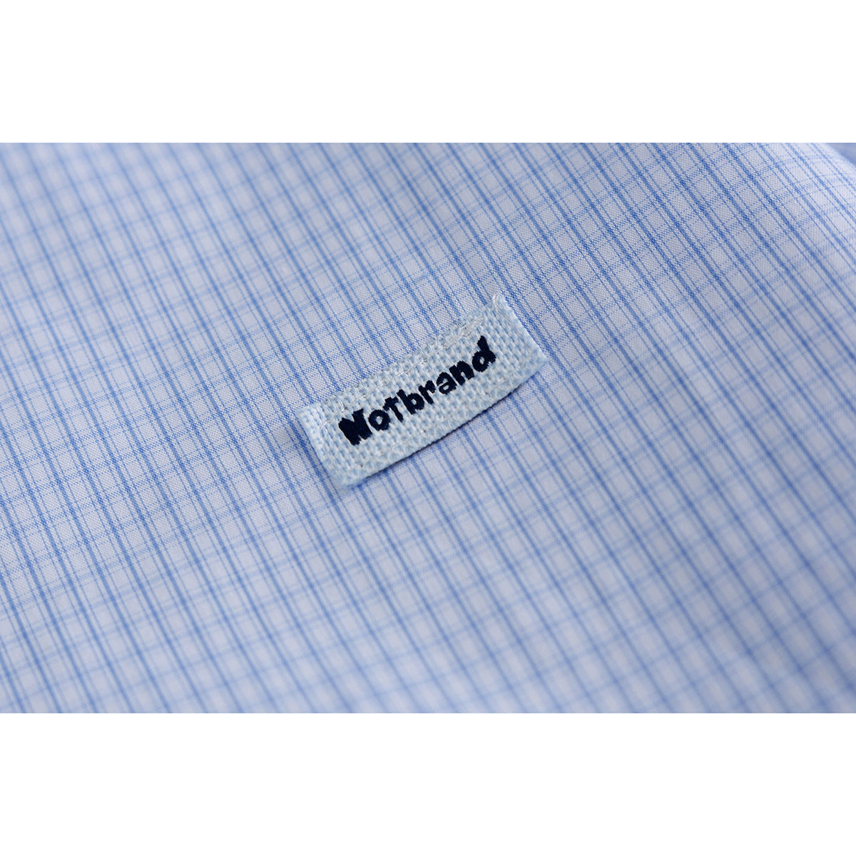 Close-up of a woven brand tab on light blue fine-check shirt fabric.