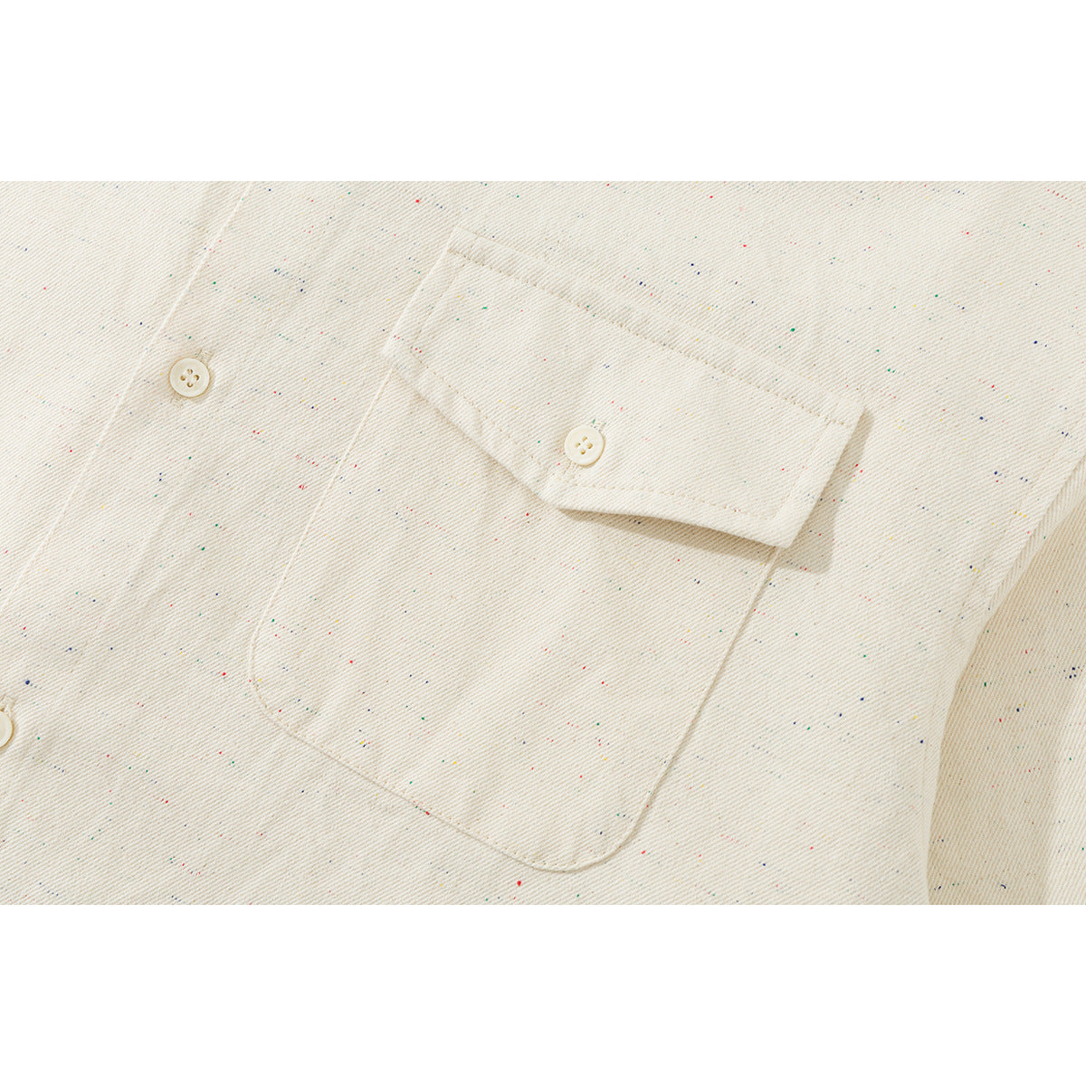 Close-up of an ivory shirt’s buttoned chest pocket and flap, with fine multicolored flecks.