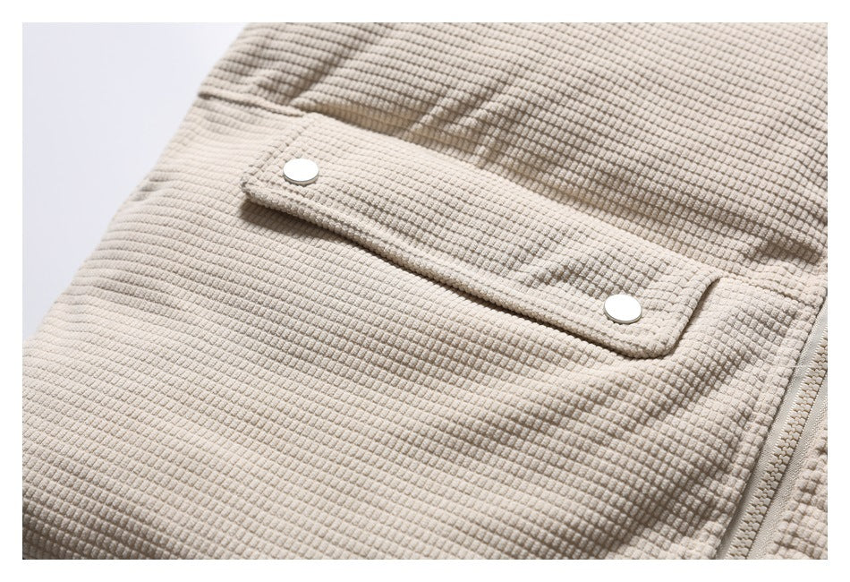 Close-up of a snap-button flap pocket and zipper on the light beige textured jacket.