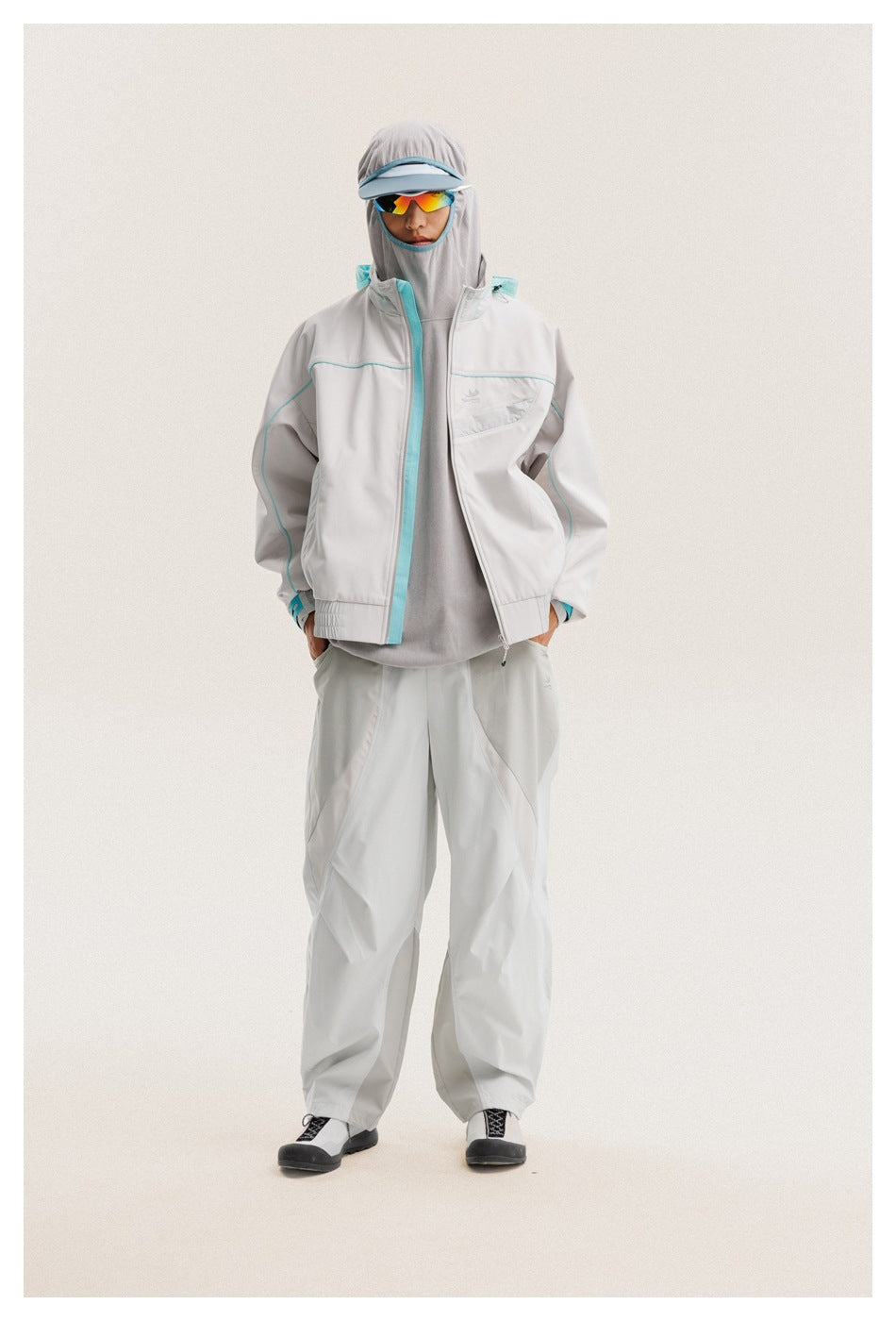 Front view of a model wearing an open light gray jacket with turquoise piping and loose matching pants.