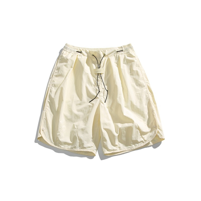 Pale sand-colored knee-length shorts with black drawcord, toggle and curved snap side hems, flat lay