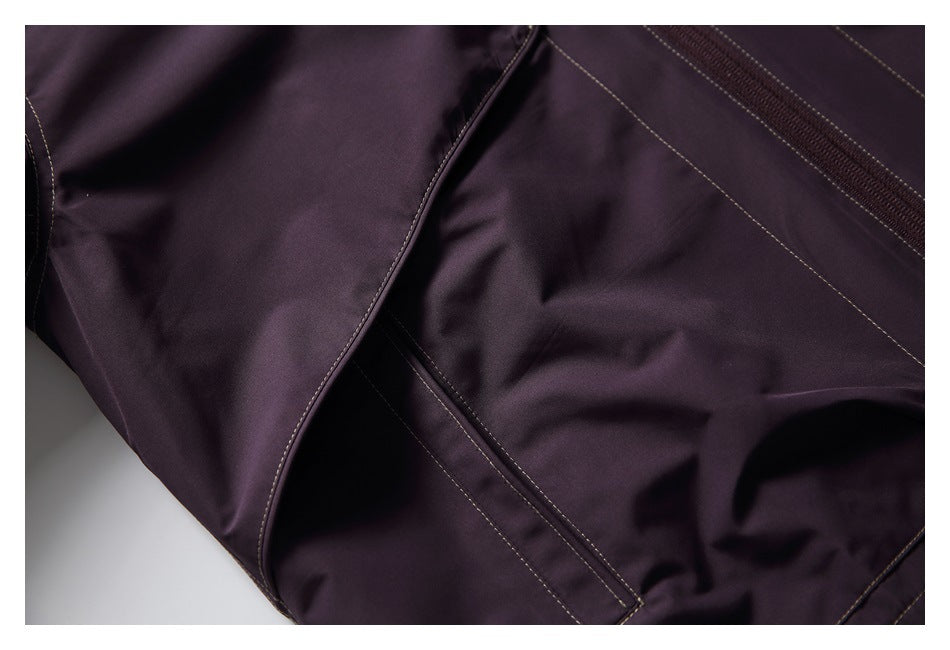 Close-up of the dark plum jacket's lower front pocket opening and contrasting topstitching.