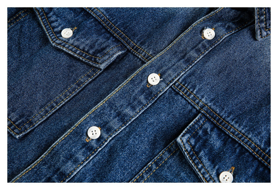 Angled close-up of dark blue denim shirt pockets and button placket with contrast stitching.