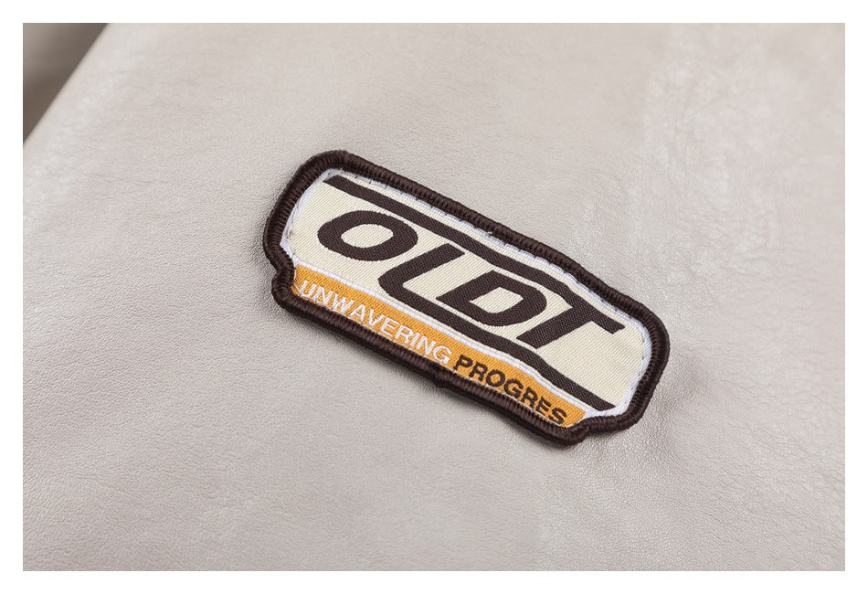Close-up of a stitched OBT patch with the words “UNWAVERING PROGRESS” on a light beige jacket.