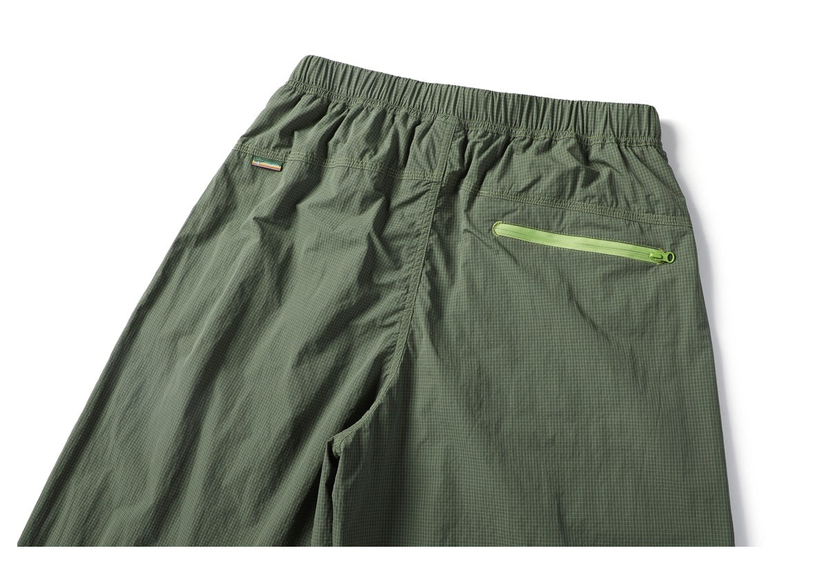 Back view of olive-green grid-patterned bottoms with an elastic waistband and a lime-green zip pocket.