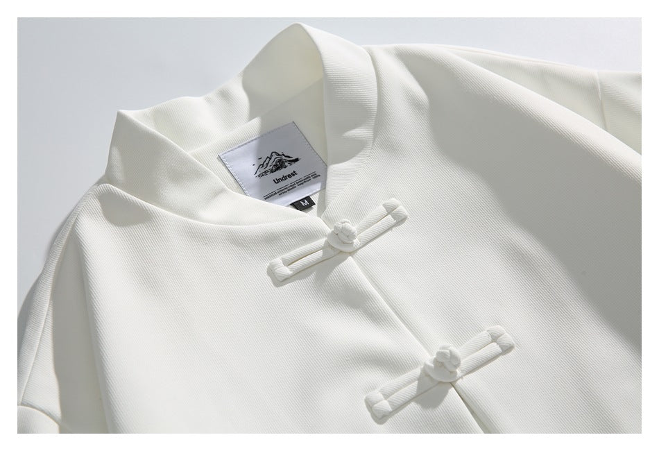 Close-up of the white jacket's stand collar, sewn-in neck label and knotted frog closures.
