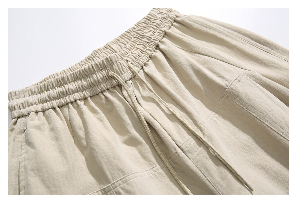 Close-up of beige pants with a gathered elastic waistband, drawstring and stitched pocket details.