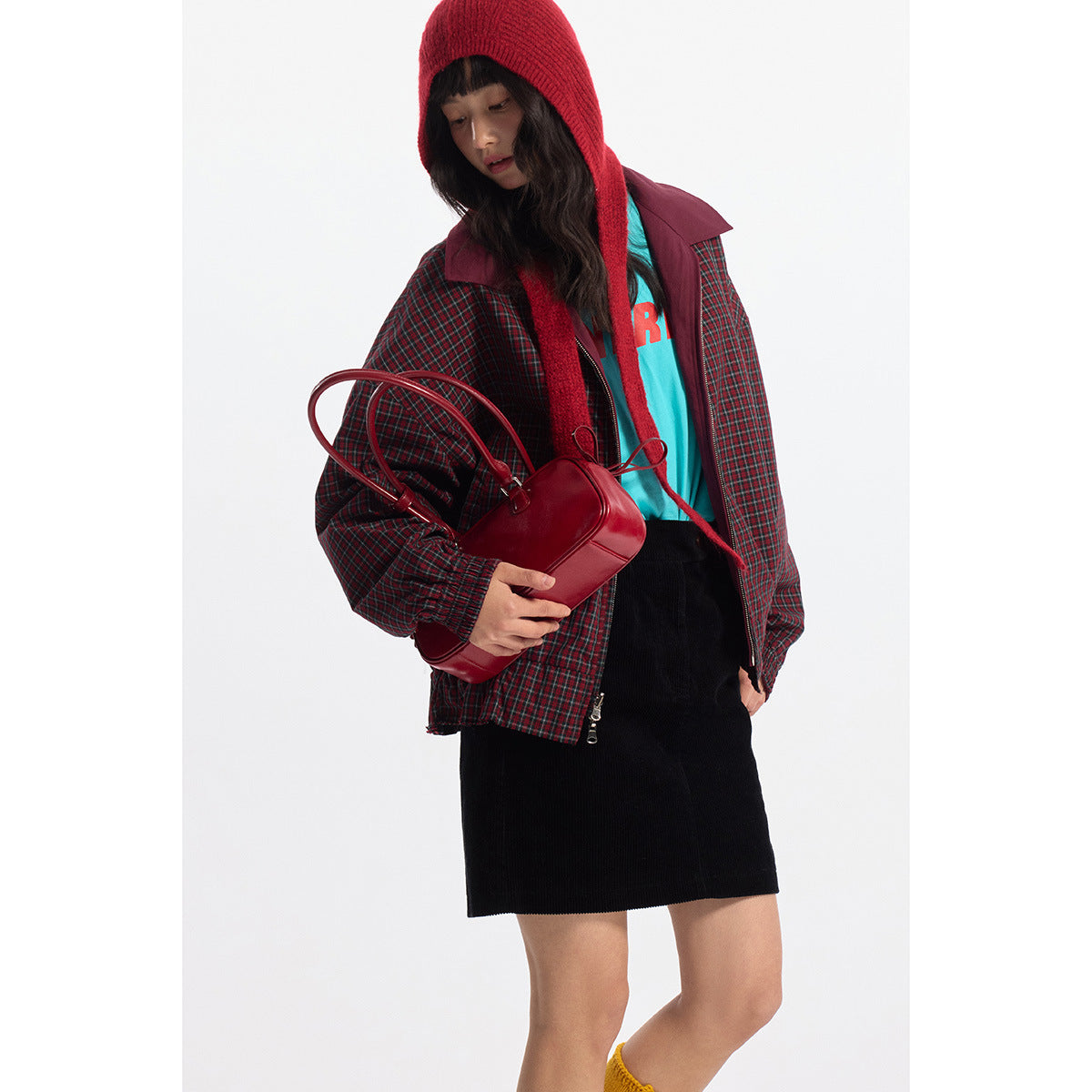 Model wearing a red-and-green plaid jacket with burgundy collar and trim, a red knit hood, and a black skirt.