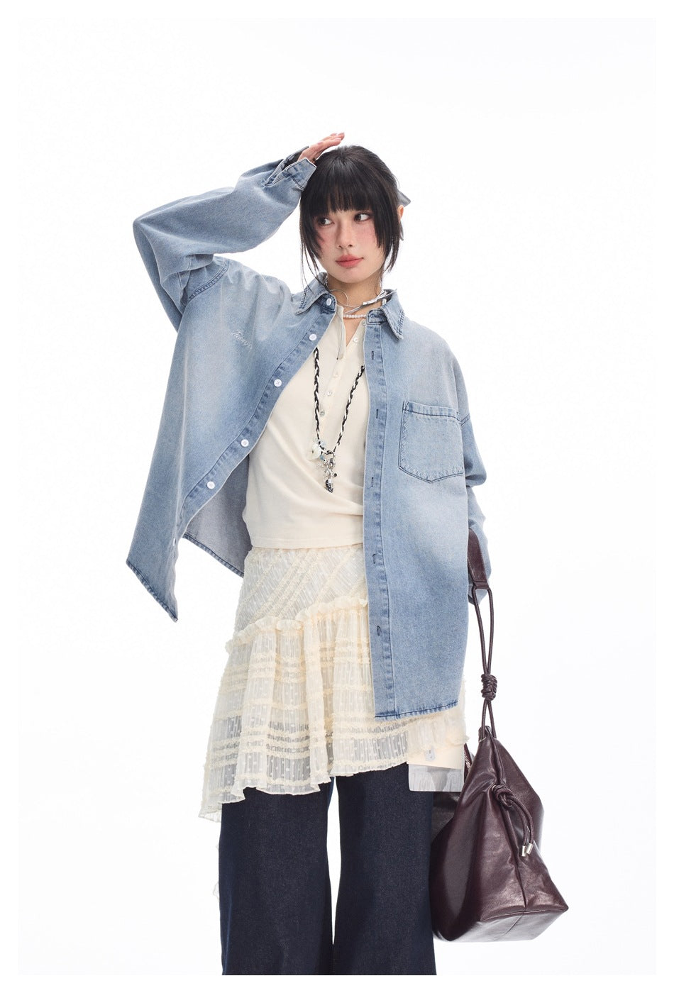 Model in a light blue oversized denim shirt over cream layers; close view shows its button front and chest pocket.