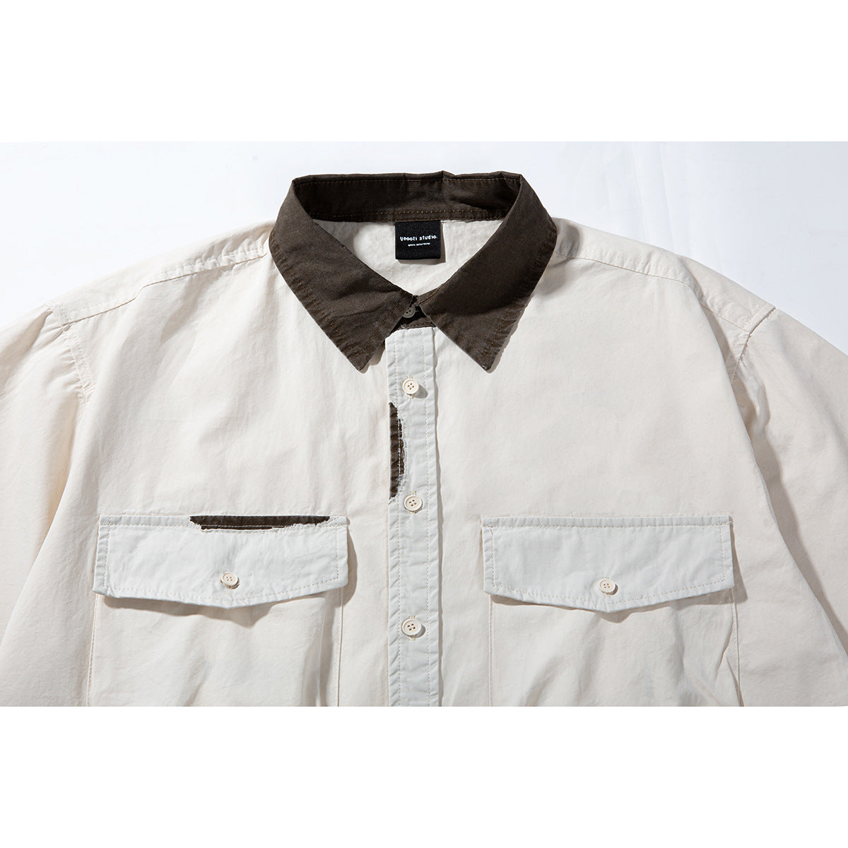 Close-up of an off-white short-sleeve shirt with a dark brown collar, button placket and two flap chest pockets.