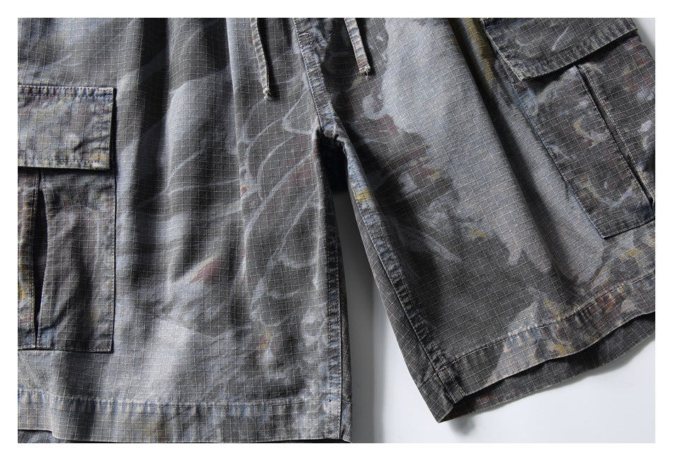 Close-up of gray patterned cargo shorts showing the leg fabric, flap pocket, seams, and hem.