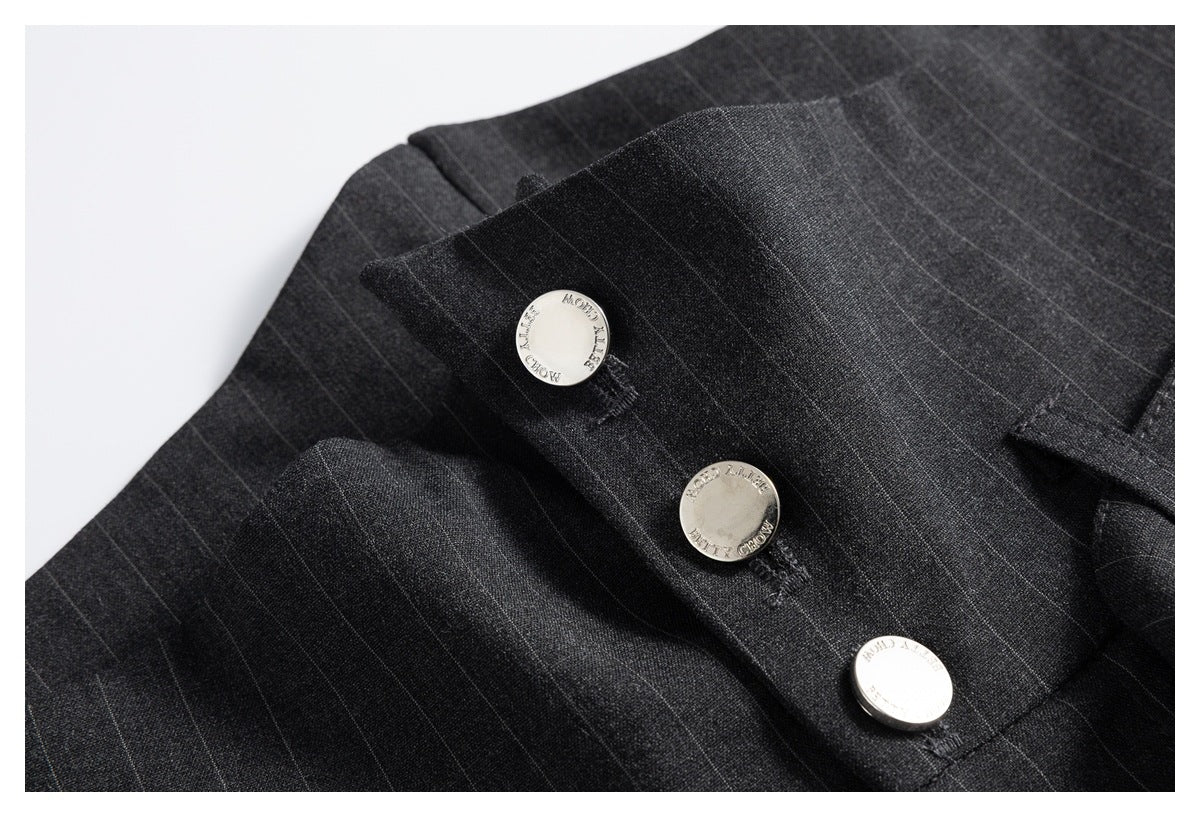 Close-up of three engraved silver buttons on the waistband of charcoal pinstripe trousers.