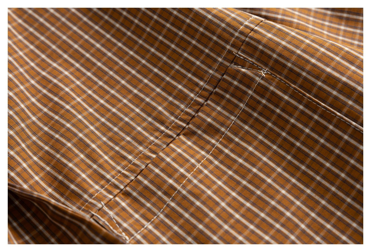 Close-up of the brown plaid shirt fabric and stitched pocket edge.