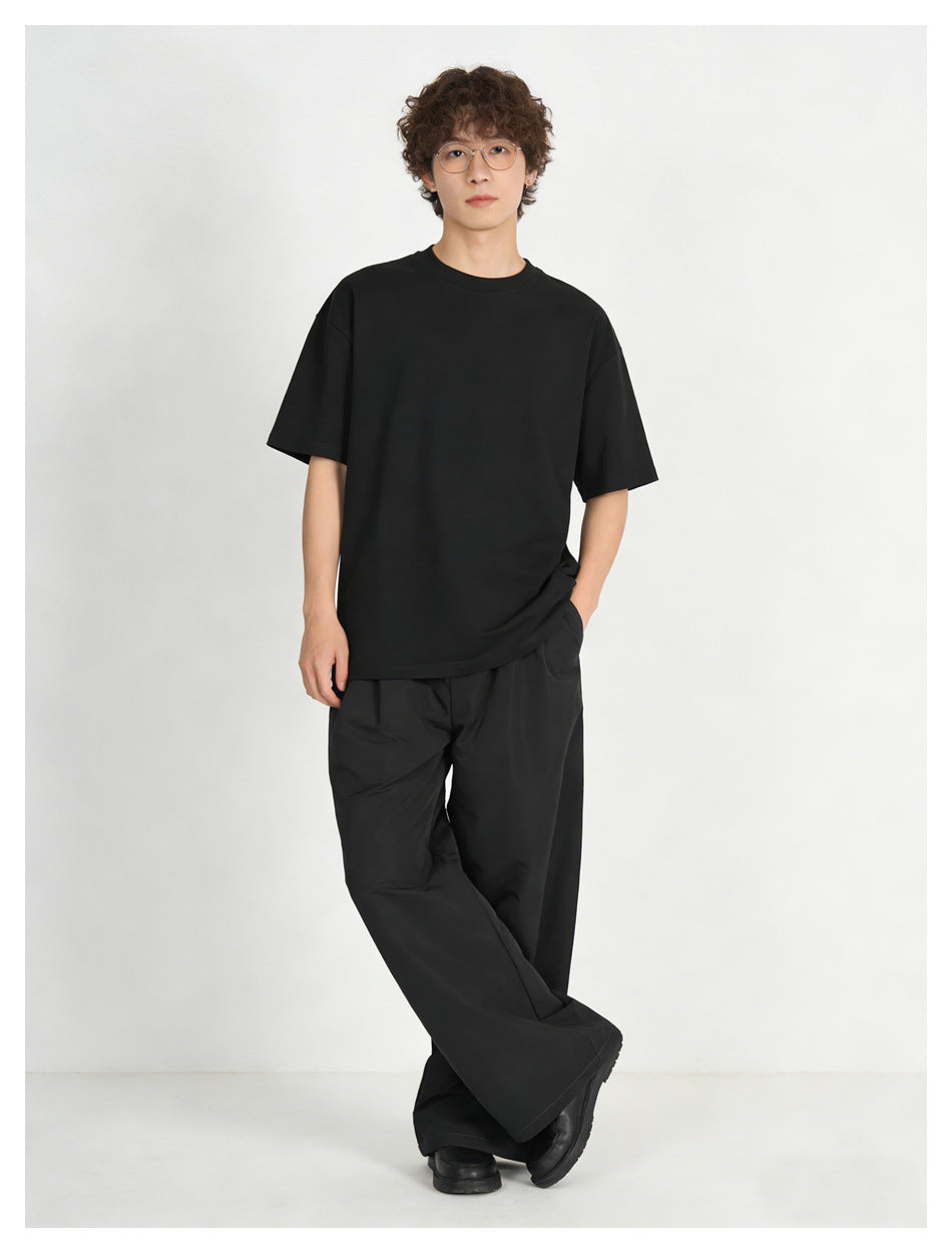 Model in black wide-leg pants and a black tee, standing front view with hand in pocket