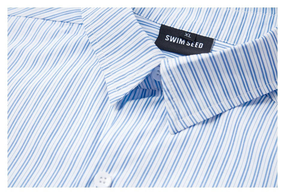 Close-up of a white shirt's pointed collar and black SWIM SEED neck label against fine blue stripes.