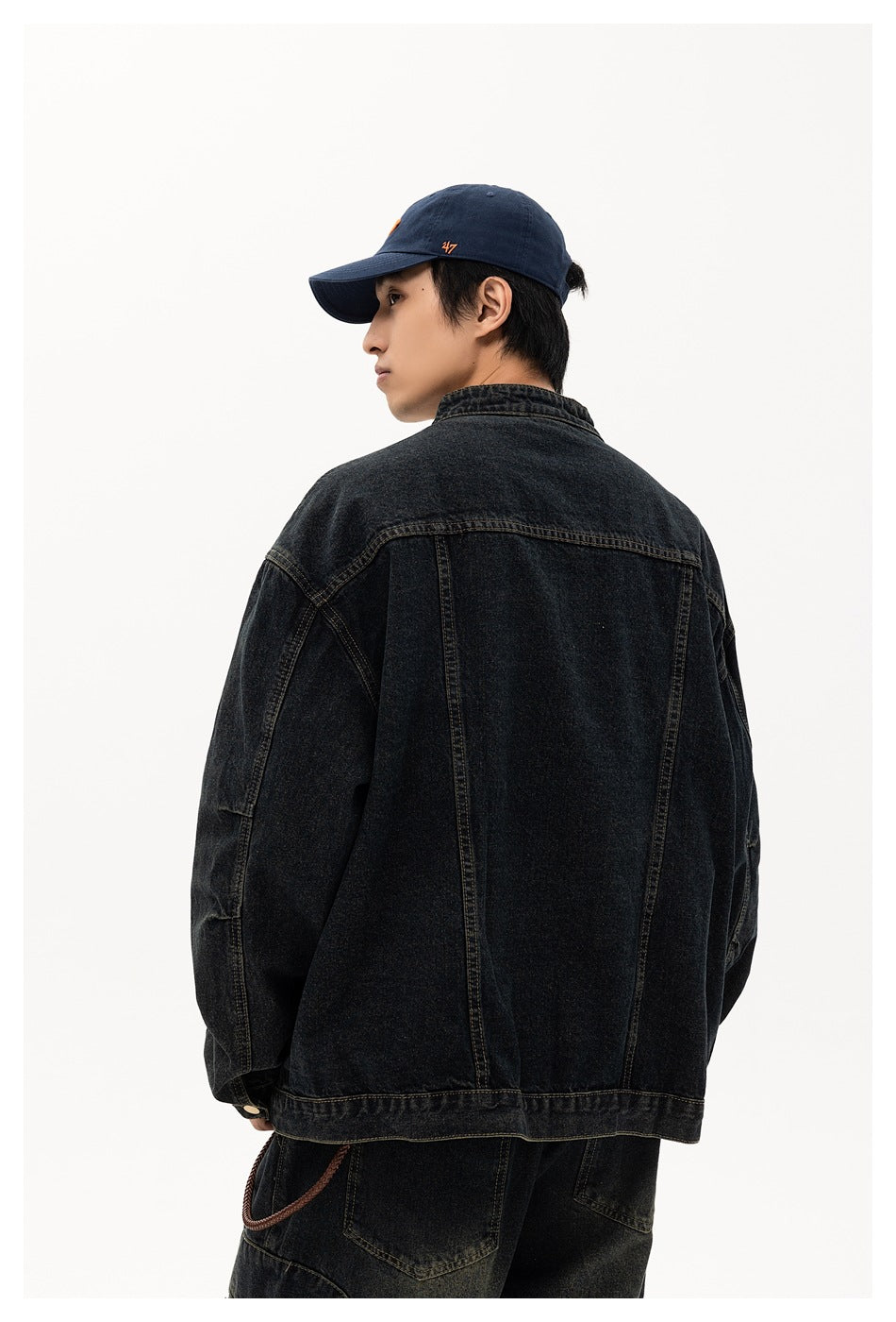 Back view of a model wearing an oversized black washed-denim jacket with panel seams.