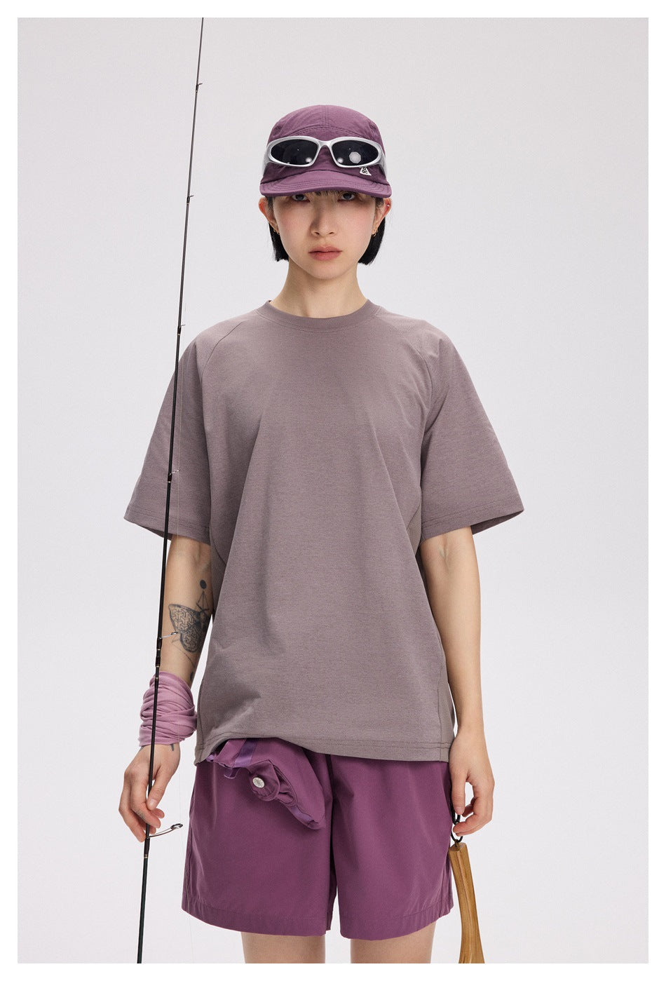 Front view of a model wearing a mauve oversized T-shirt and purple shorts, with a purple cap and sunglasses.