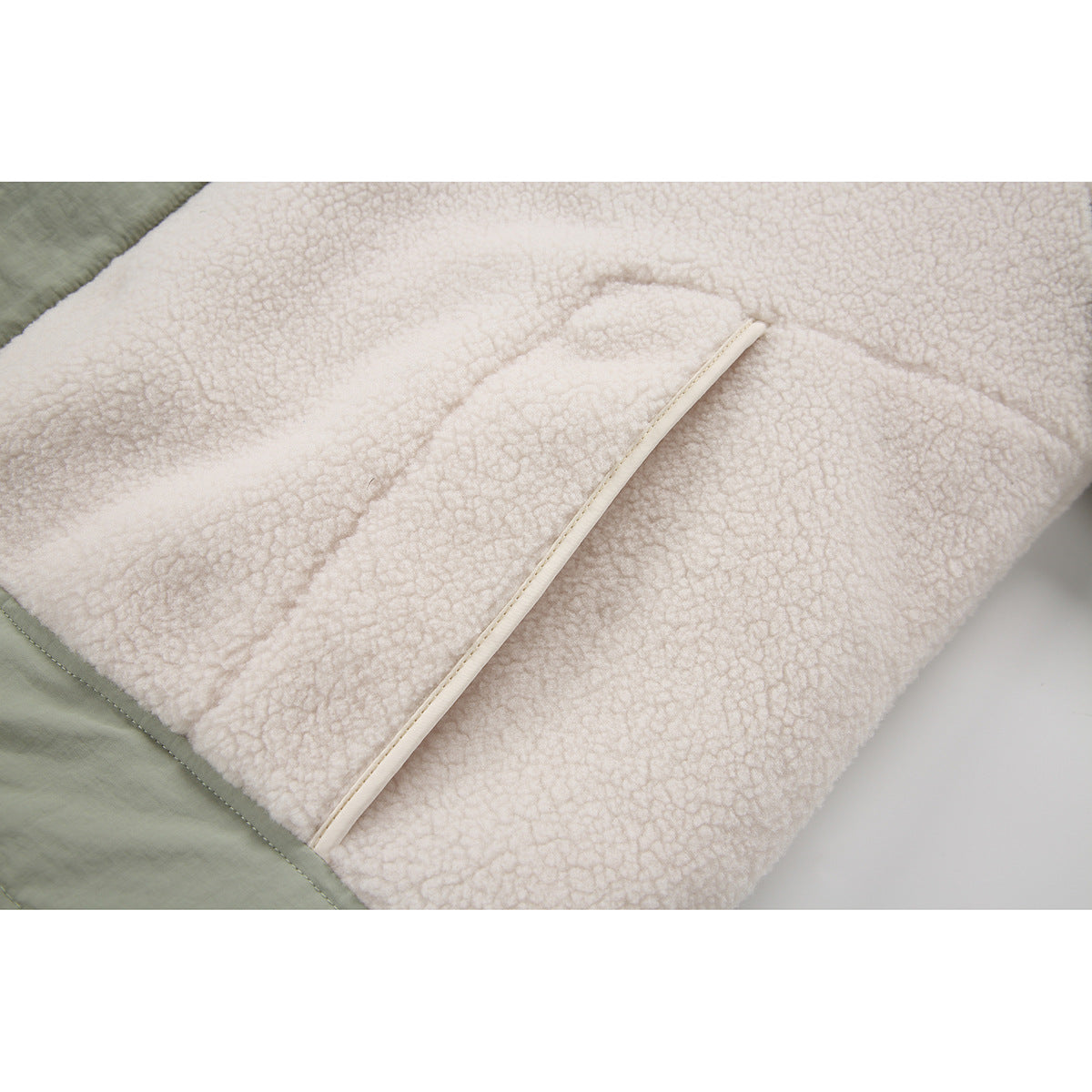 Close-up of cream textured fleece and a piped pocket edge, bordered by sage-green fabric.