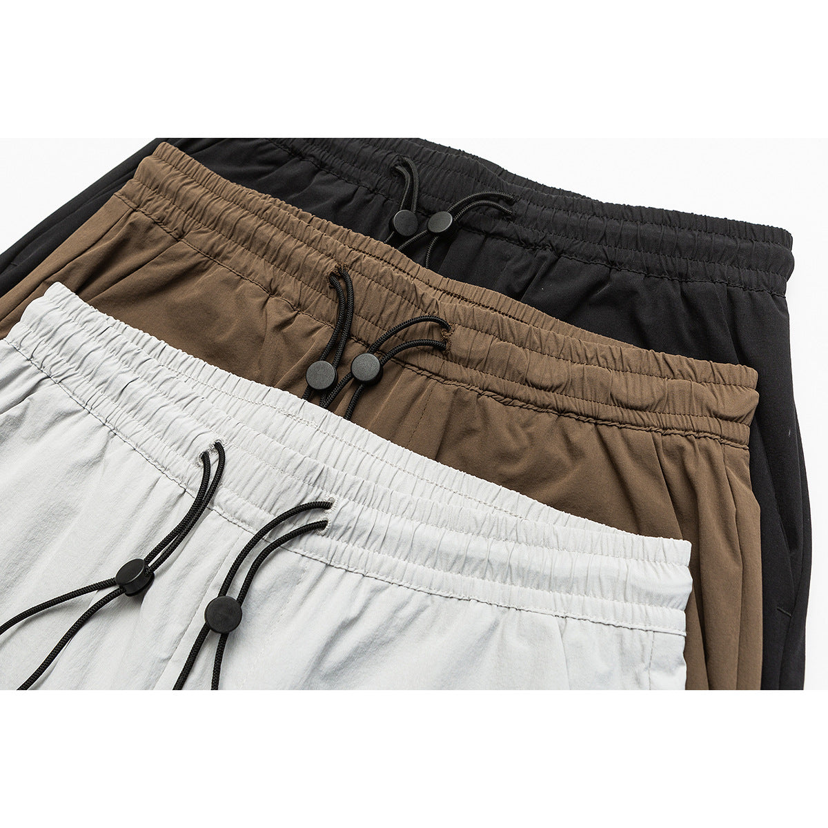 Close-up of light gray, taupe, and black trousers with elastic drawstring waistbands.