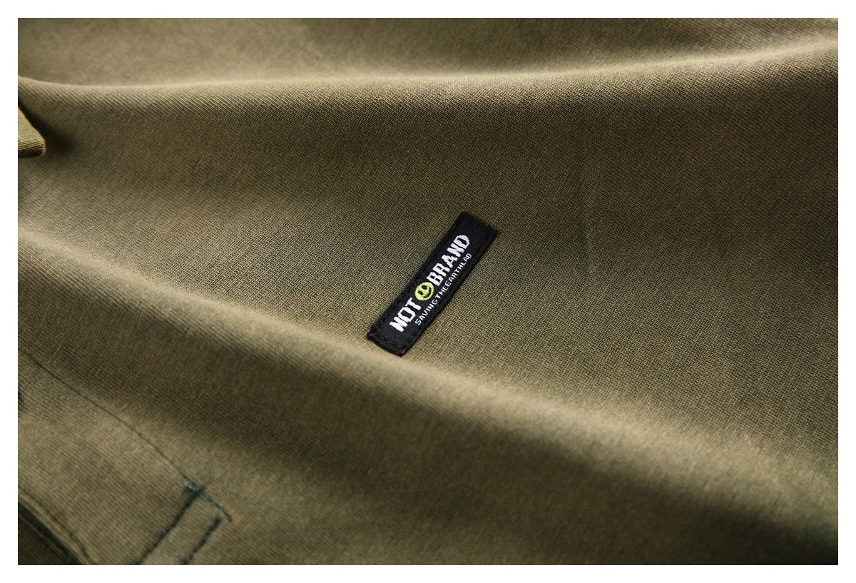 Close-up of olive-green shirt fabric with a small black sewn logo patch.
