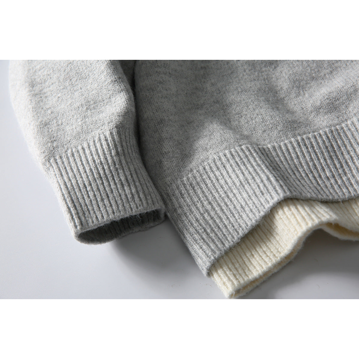 Close-up of gray sweater sleeve cuff and ribbed hem, with a cream knit layer underneath.