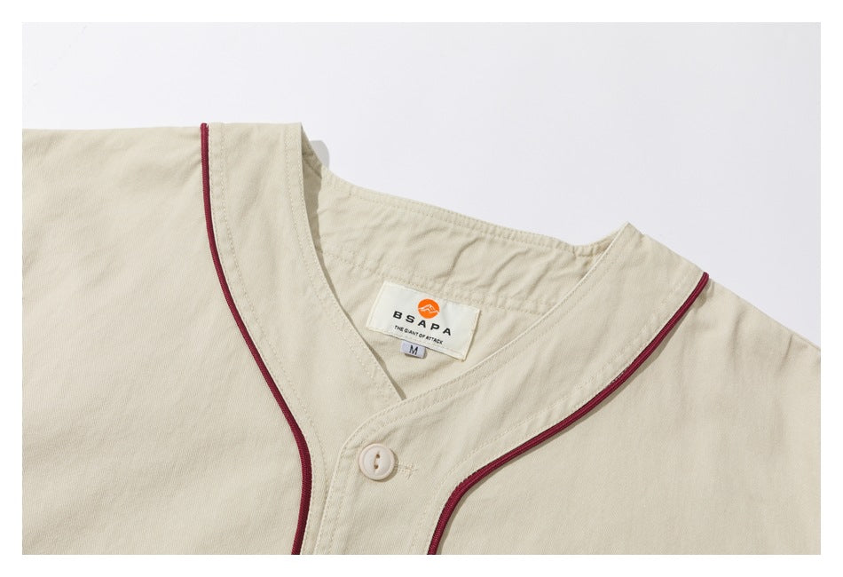 Close-up of an ivory garment neckline with burgundy piping, a button, and a sewn brand label.
