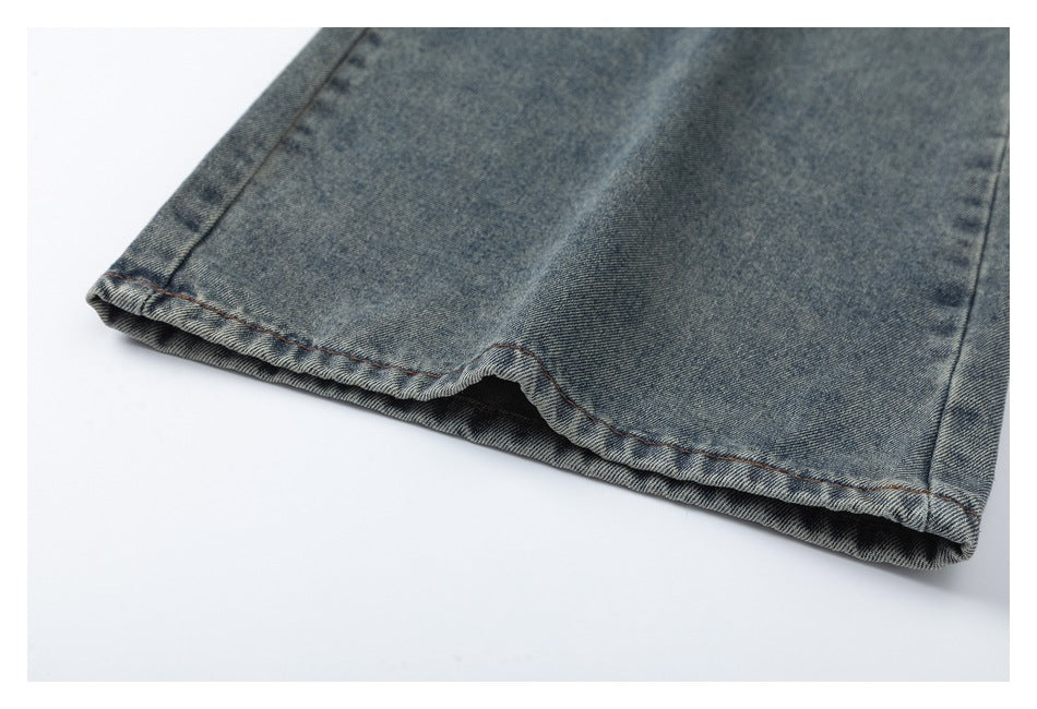 Close-up of the stitched hem at the leg opening of faded blue-gray jeans.