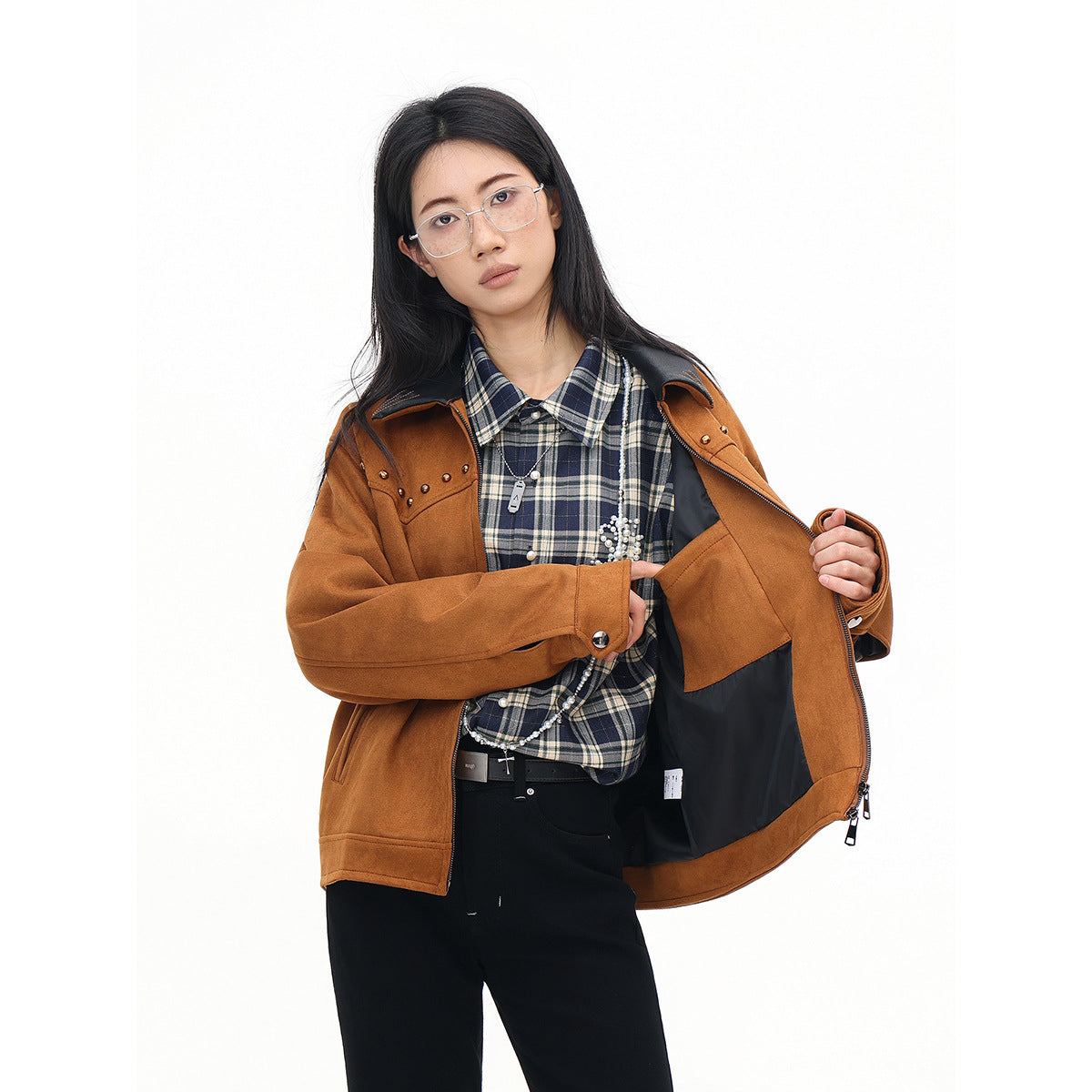 Model opens a rust-brown jacket to show its black lining, worn over a navy plaid shirt and black trousers.